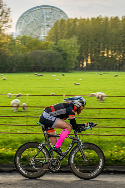Cyclist in NTC kit on time trial bike with Jodrell Bank in background
