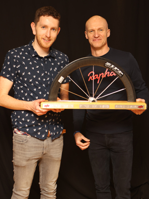 A man receives a trophy - made of half a wheel - from another man