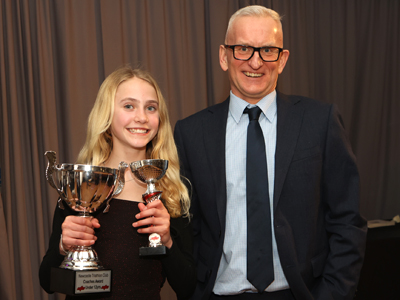 A girl holding two trophies, and a man, both smiling